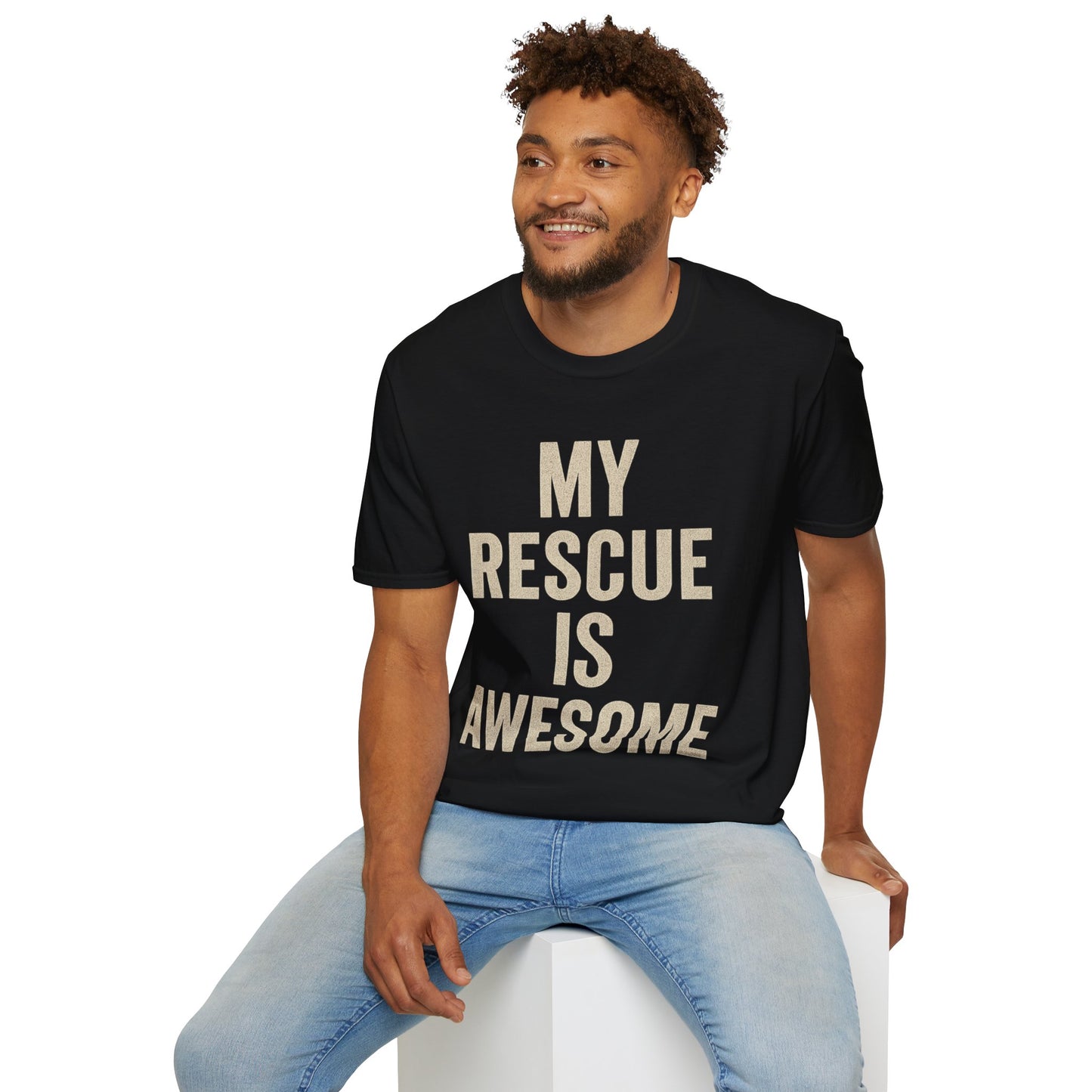 Black unisex t-shirt worn by a seated male model, featuring the phrase "My Rescue Is Awesome" in large, distressed cream text. The model is smiling and wearing light blue jeans, creating a relaxed and confident dog-rescue supporter look.