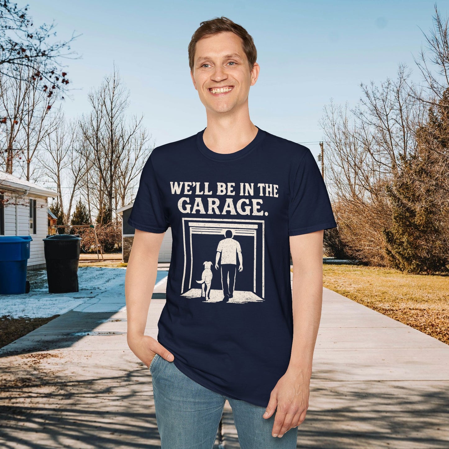 Person wearing a navy blue t-shirt with 'WE'LL BE IN THE GARAGE' text and graphic, standing outdoors.