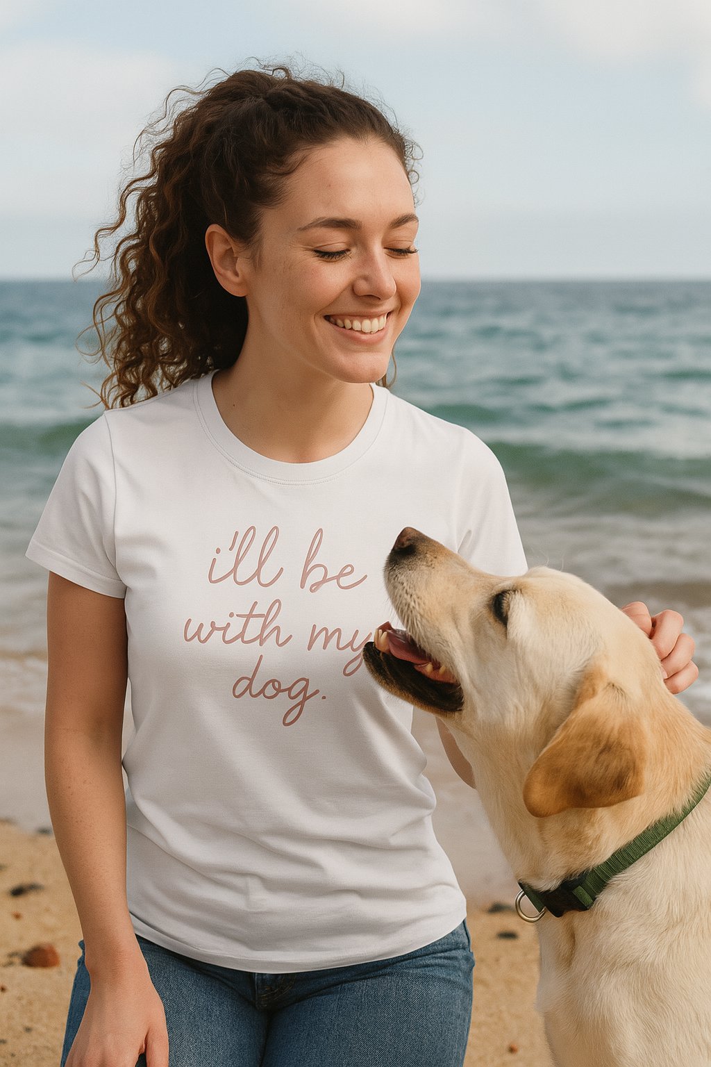 Woman wearing a t-shirt with 'I'll be with my dog' on a beach with a dog.