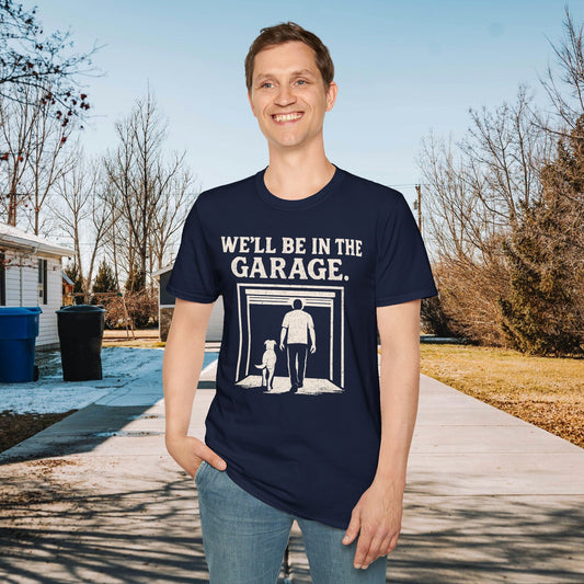 Person wearing a navy blue t-shirt with 'WE'LL BE IN THE GARAGE' text and graphic, standing outdoors.