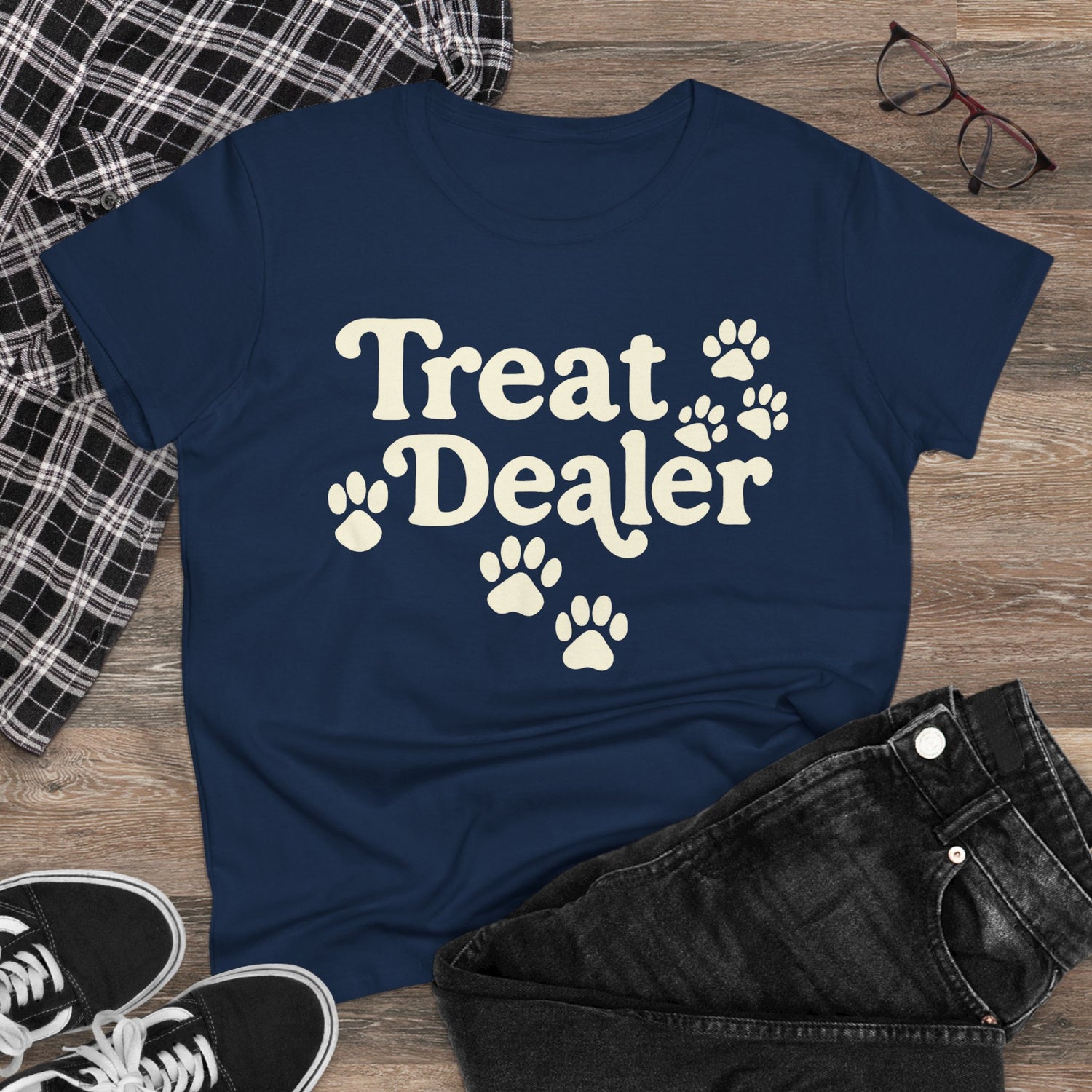 Navy blue t-shirt with 'Treat Dealer' text and paw prints on a wooden surface with casual items.