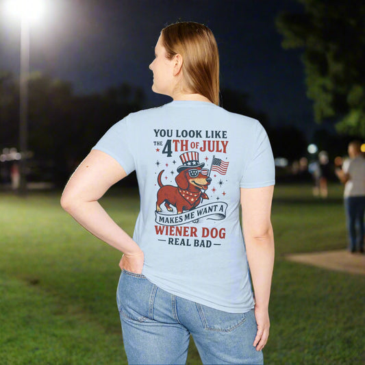 Woman wearing a light blue t-shirt with a patriotic dachshund graphic on the back. Text reads “You look like the 4th of July — makes me want a wiener dog real bad.” The dog is wearing sunglasses, a top hat, and holding an American flag.

