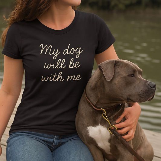 Person wearing a black t-shirt with 'My dog will be with me' text, holding a dog by a body of water.