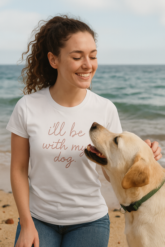 Woman wearing a t-shirt with 'I'll be with my dog' on a beach with a dog.