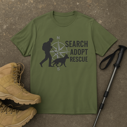 Olive green t-shirt featuring a black silhouette of a person walking a dog in front of a gray compass rose, with bold text reading "SEARCH ADOPT RESCUE" stacked on the right.








