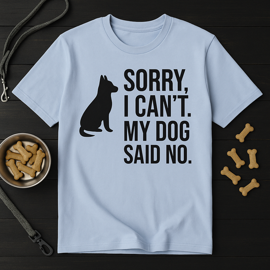 Light blue t-shirt with bold black print that reads “Sorry, I Can’t. My Dog Said No.” next to a black dog silhouette. Shirt is crumpled slightly for texture and shown against a dark background with neutral props, making the design the visual focus.

